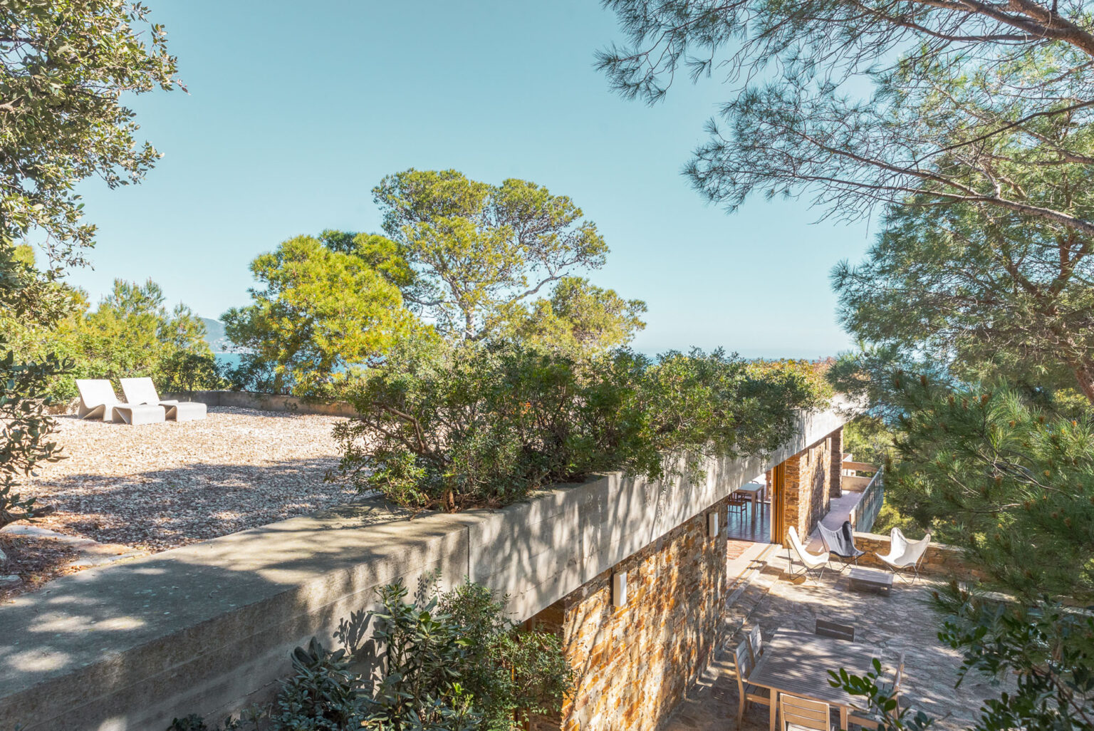 A modern stone villa among pines, its terrace looking over the sea